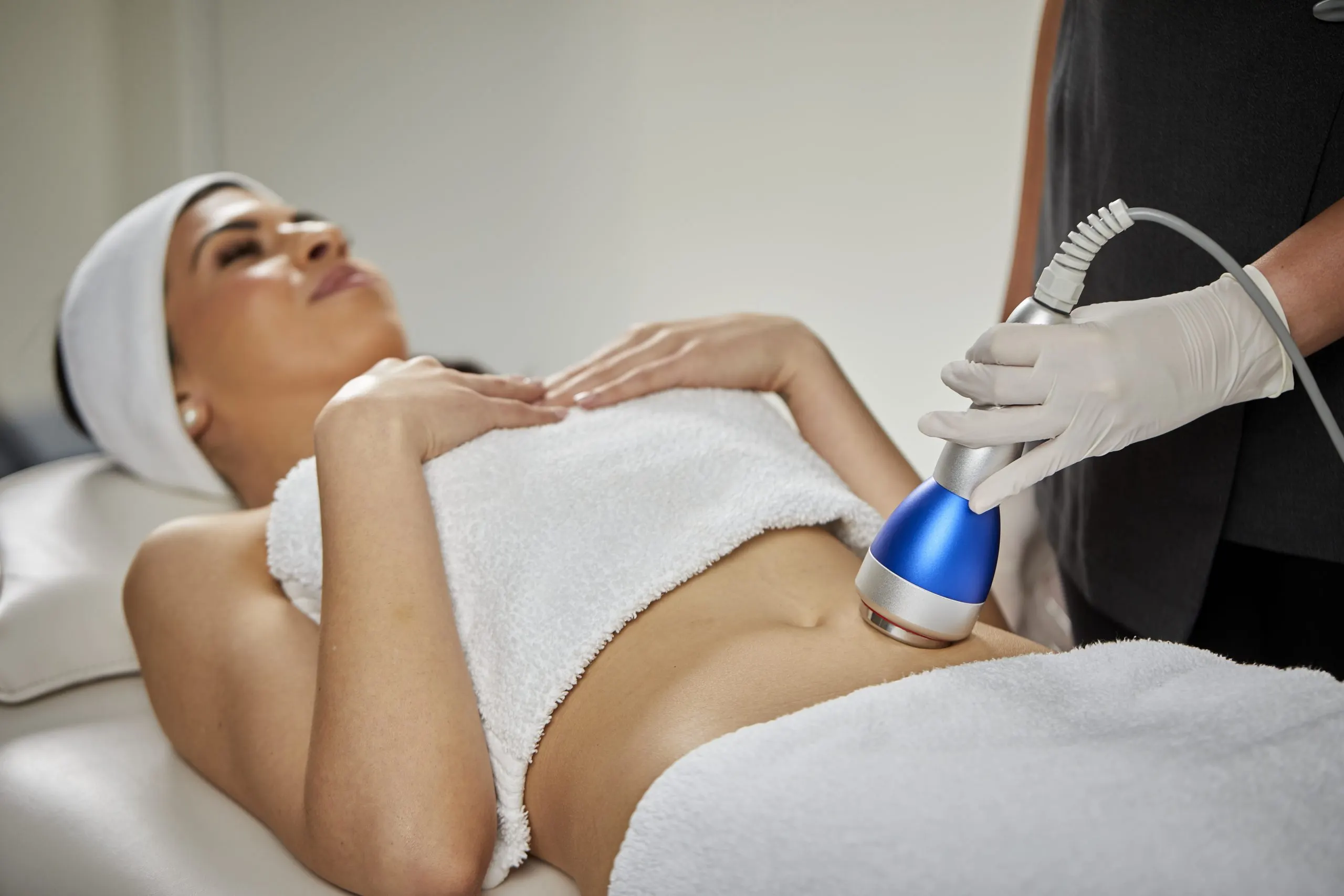 Clinician uses device on woman's abdomen for body treatment.